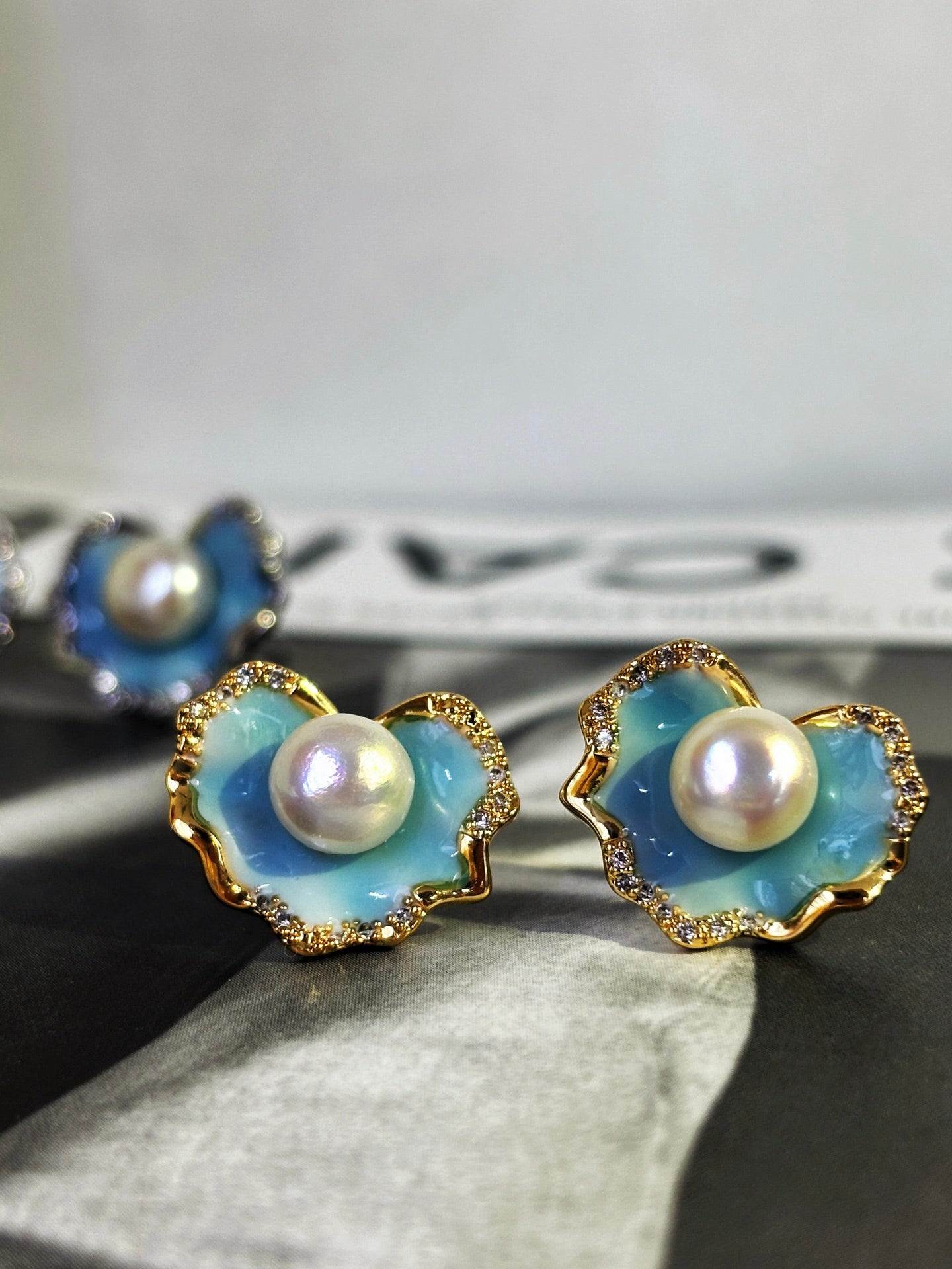 A pair of glacier blue enamel stud earrings featuring 8mm natural freshwater pearls and sterling silver posts.