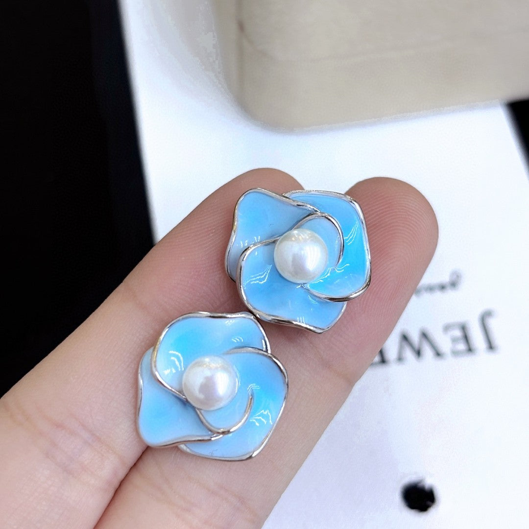 Blue enamel camellia stud earrings with a central freshwater pearl on sterling silver posts.