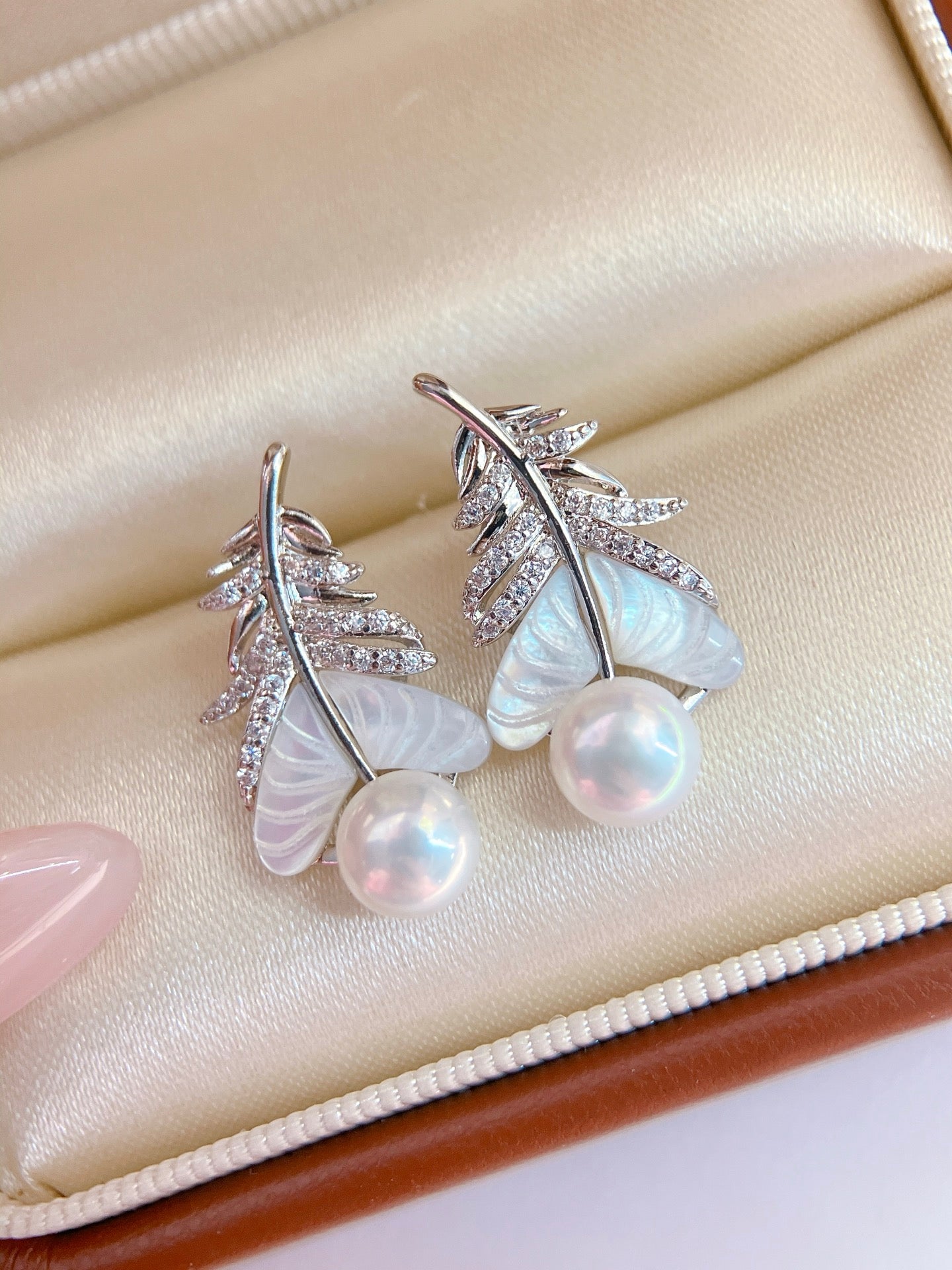 Close-up of feather-inspired pearl earrings
Pearl stud with feather detail and mother-of-pearl finish