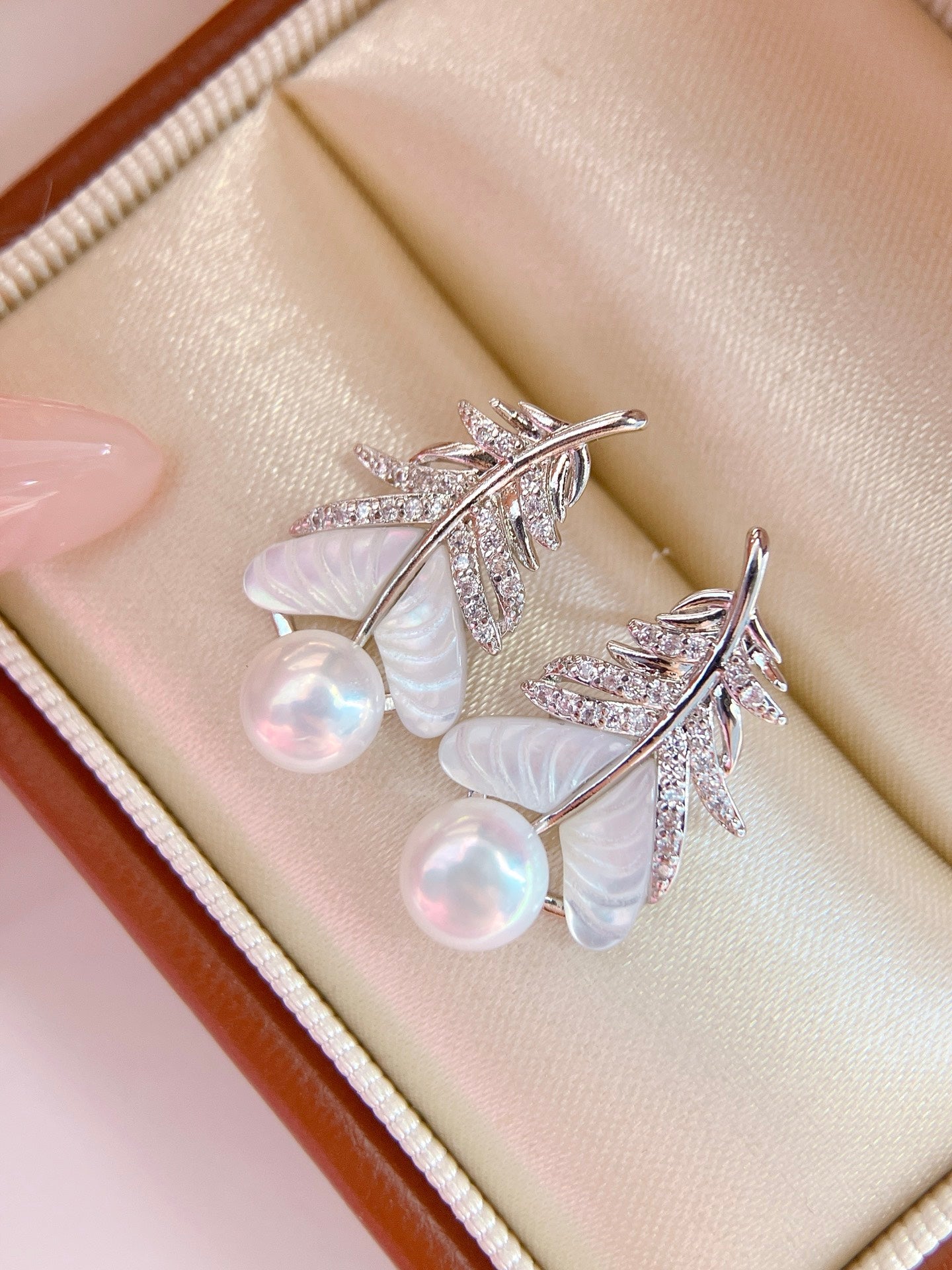 Close-up of feather-inspired pearl earrings
Pearl stud with feather detail and mother-of-pearl finish