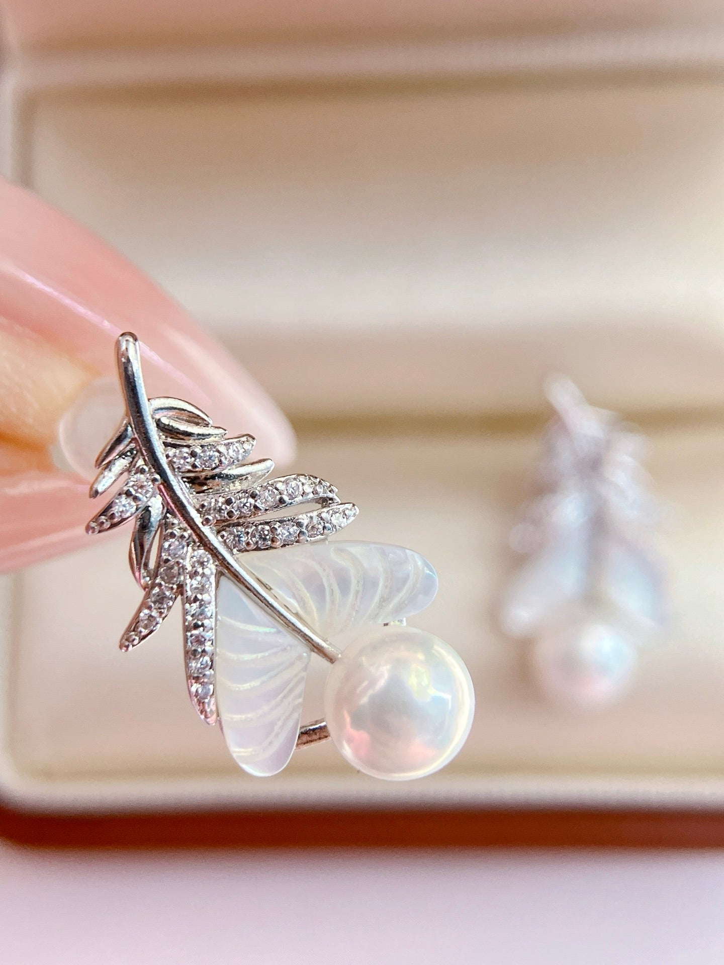 Close-up of feather-inspired pearl earrings
Pearl stud with feather detail and mother-of-pearl finish