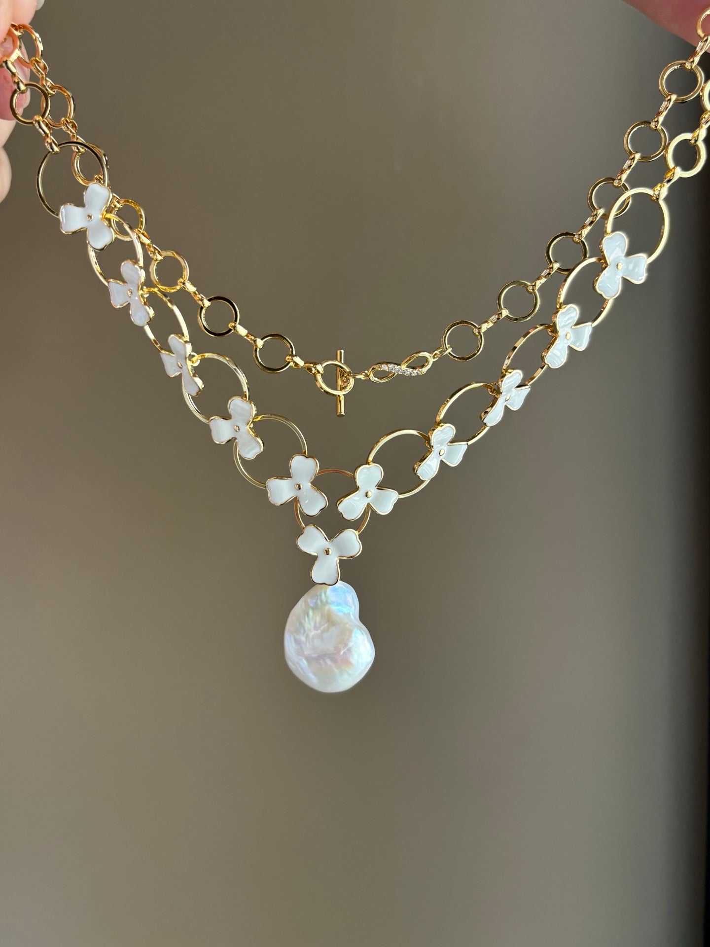 Layered baroque pearl necklace with donut and clover floral accents on white background