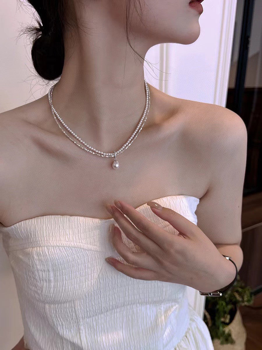 Model wearing layered silver and pearl necklace with soft glow