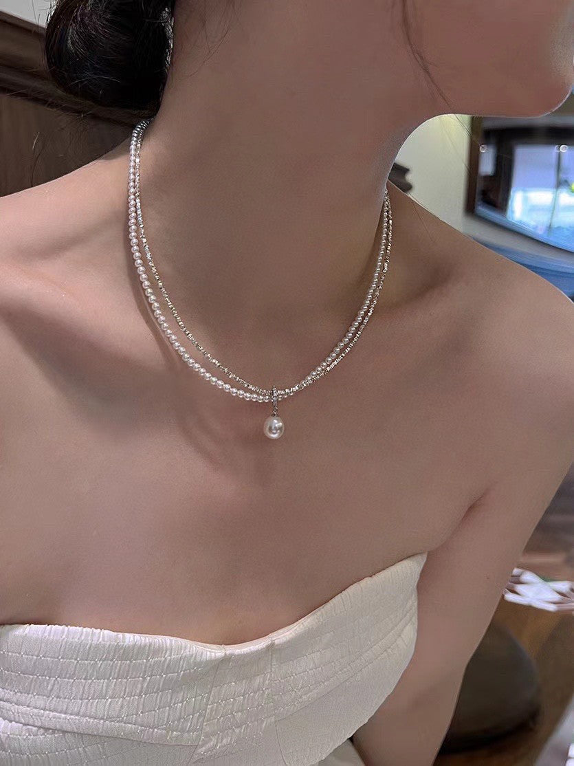 Model wearing layered silver and pearl necklace with soft glow
