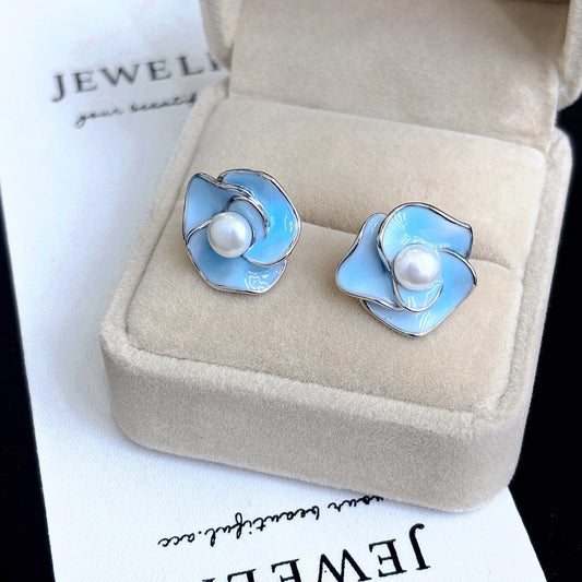 Blue enamel camellia stud earrings with a central freshwater pearl on sterling silver posts.