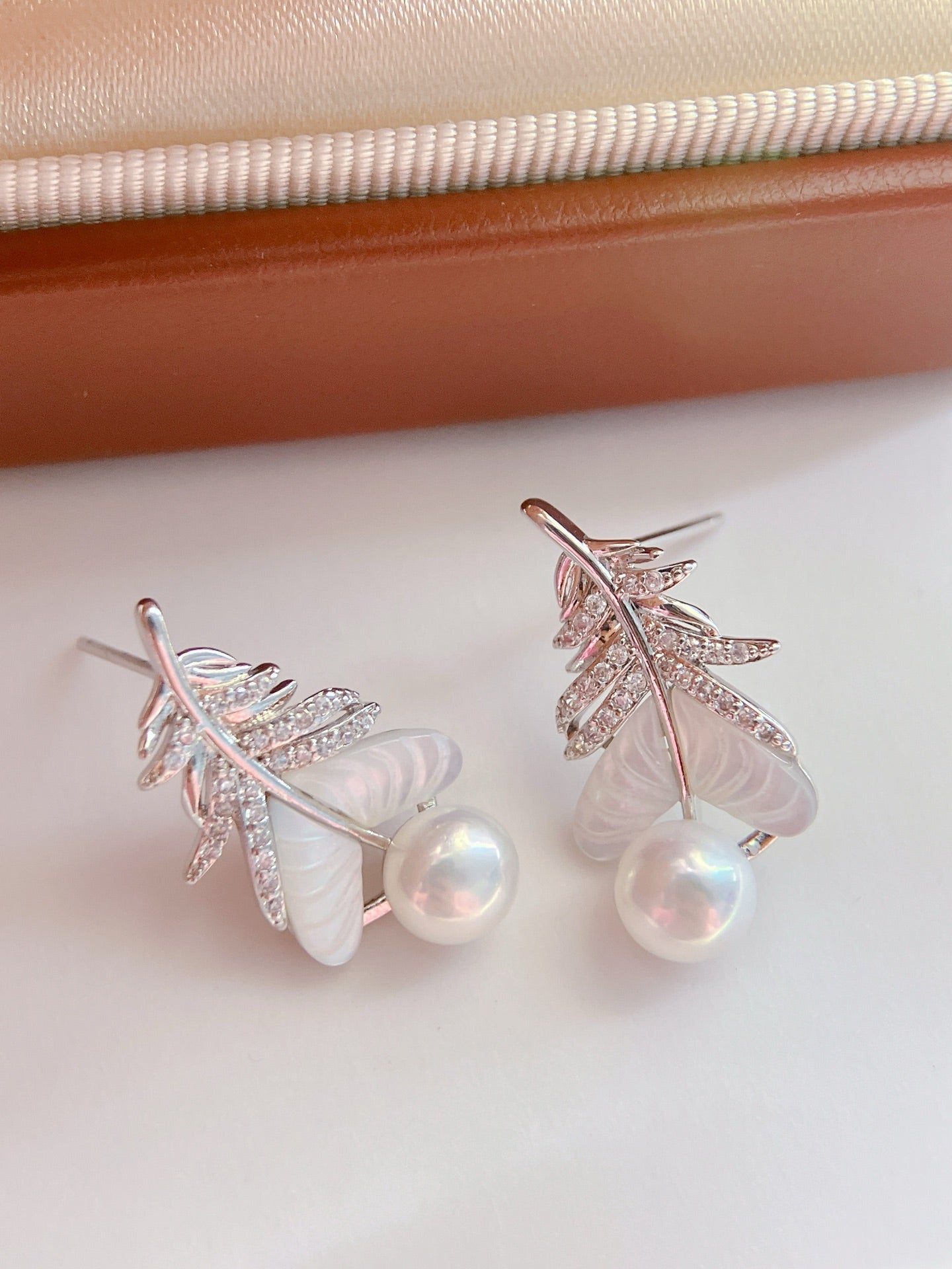 Close-up of feather-inspired pearl earrings
Pearl stud with feather detail and mother-of-pearl finish