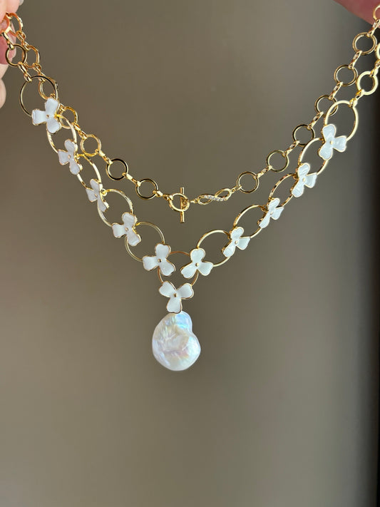 Layered baroque pearl necklace with donut and clover floral accents on white background
