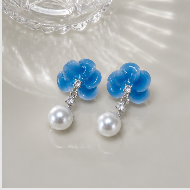 Pair of blue ice porcelain blossom pearl studs in a product-only silk and glass still life